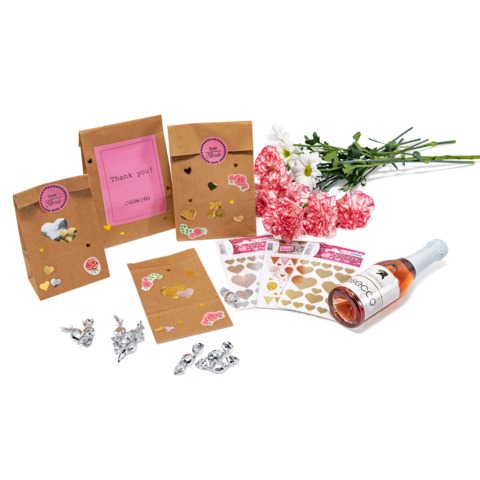 Geschenktüten mit Aufklebern, eine Flasche Sekt, Blumen und Herzaufkleber auf einem Tisch arrangiert.