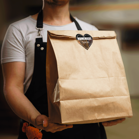 Eine Person hält eine braune Papiertüte mit einem Aufkleber, der "Homemade Spices" zeigt.