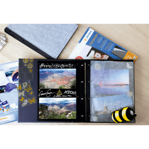 Ein offenes Fotoalbum mit Bildern von Landschaften, einem Geburtstagsgruß und dekorativen Elementen. Daneben liegt eine Fotopapierpackung.